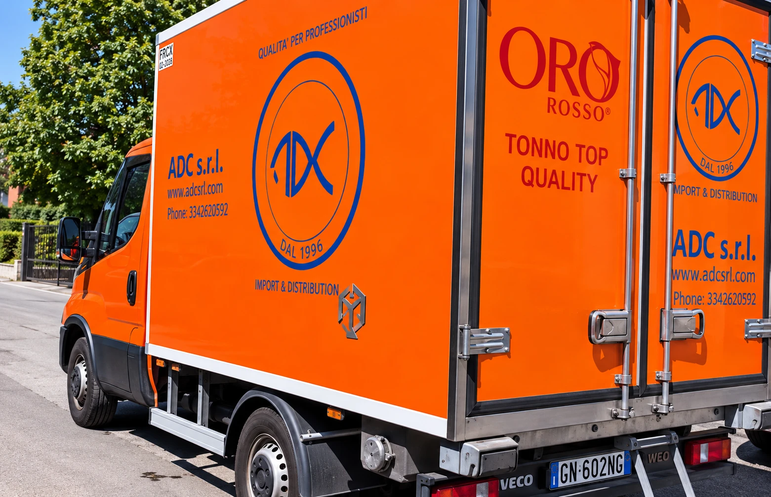 Fianco di un furgone frigorifero arancione ADC con il logo ADC, il marchio Oro Rosso «Tonno Top Quality» e la scritta Import & Distribution