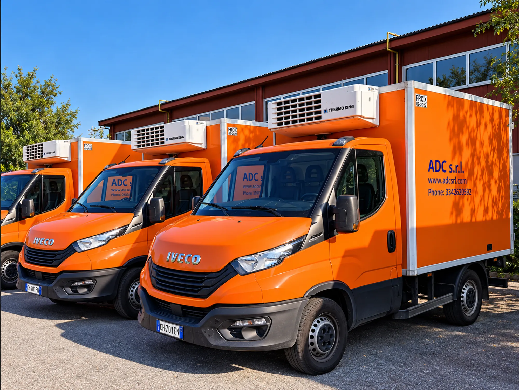 Orange ADC refrigerated vans parked in front of the warehouse, with cooling units on the roof and “ADC s.r.l.” on the body