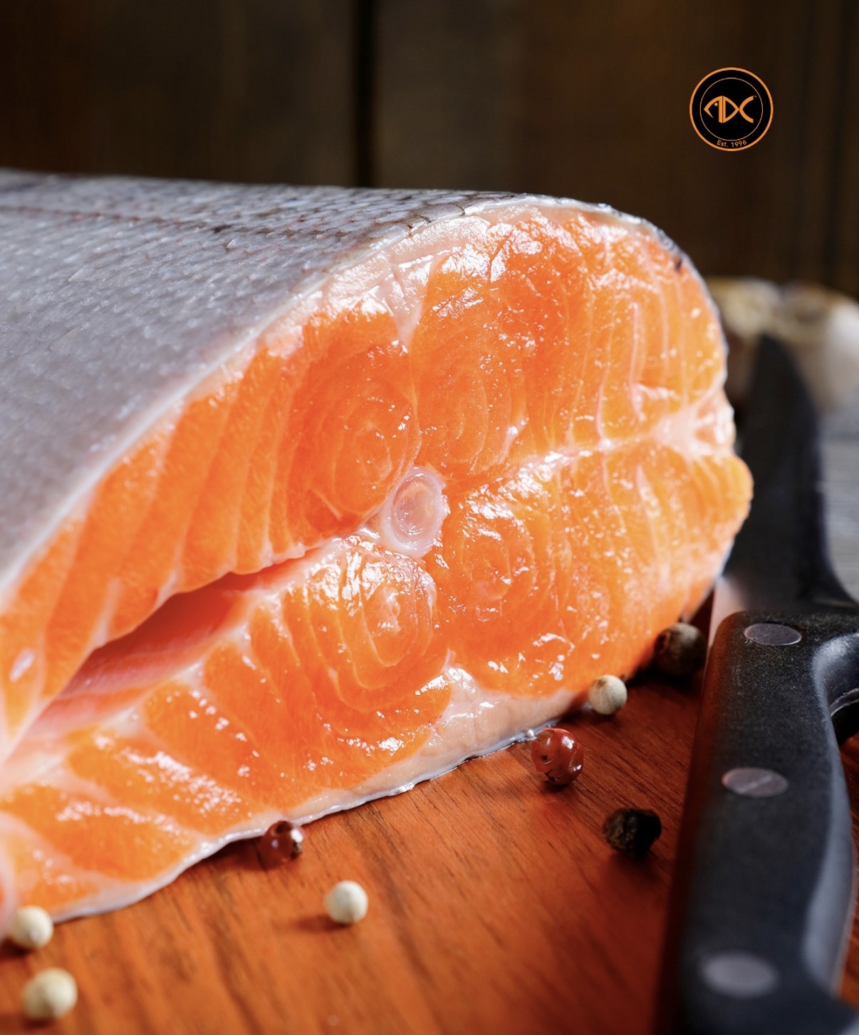 Trancio di salmone fresco su tagliere di legno, con grani di pepe e coltello